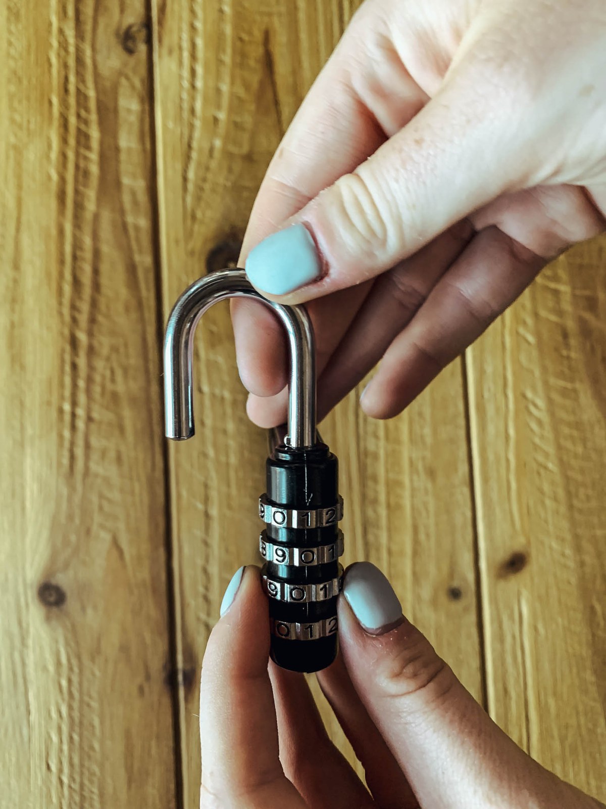 An open number lock hold by women hand in front of a wooden wall.